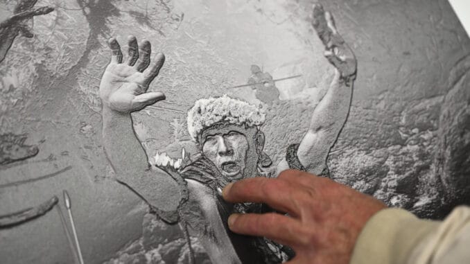 La imagen muestra la mano de una persona, percibiendo a través del tacto una fotografía de un hombre con las manos levantadas. Fuente: Computer Hoy