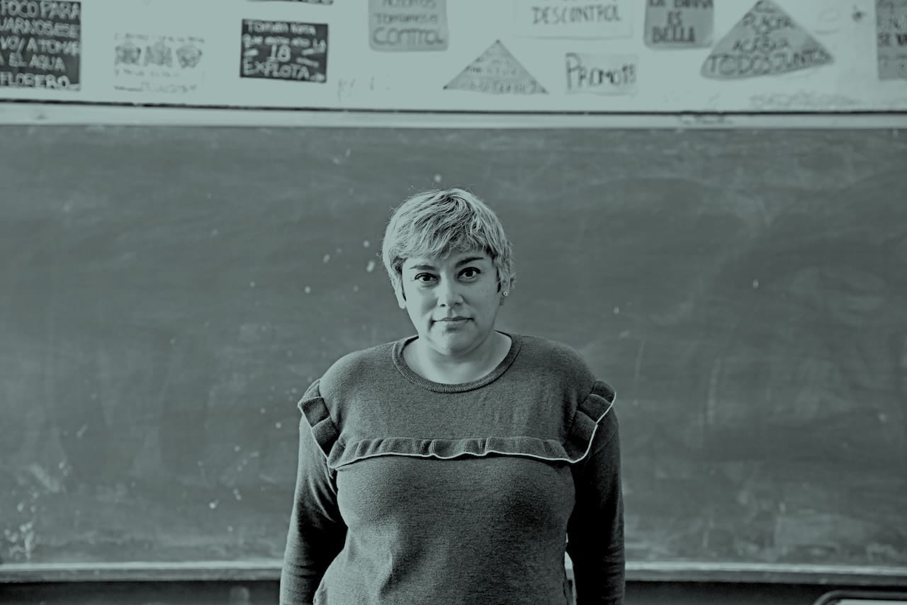 La imagen muestra una fotografía en blanco y negro de la escritora Silvana Corso delante de un pizarrón. Fuente: La Nación