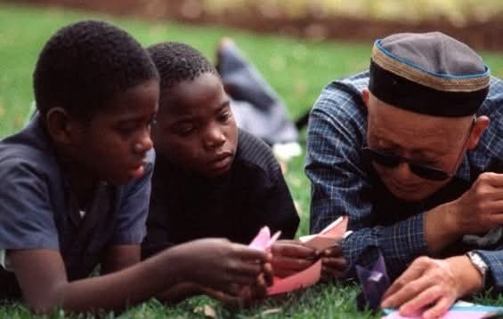Saburo Kase junto a dos niños a su derecha enseñándoles a hacer origami. Foto sacada de la página de Facebook Saburo Kase – Origami by touch