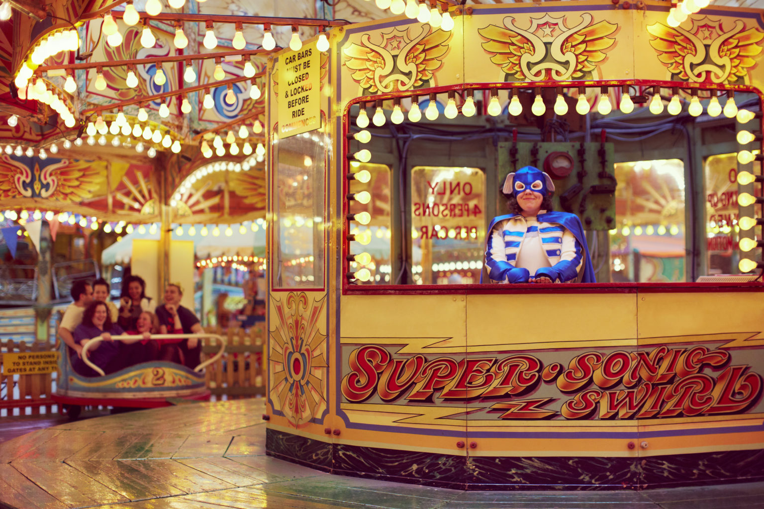 La fotografía muestra a Jess Tom vestida de superhéroe sentada detrás de un mostrador de estilo circense o de feria.