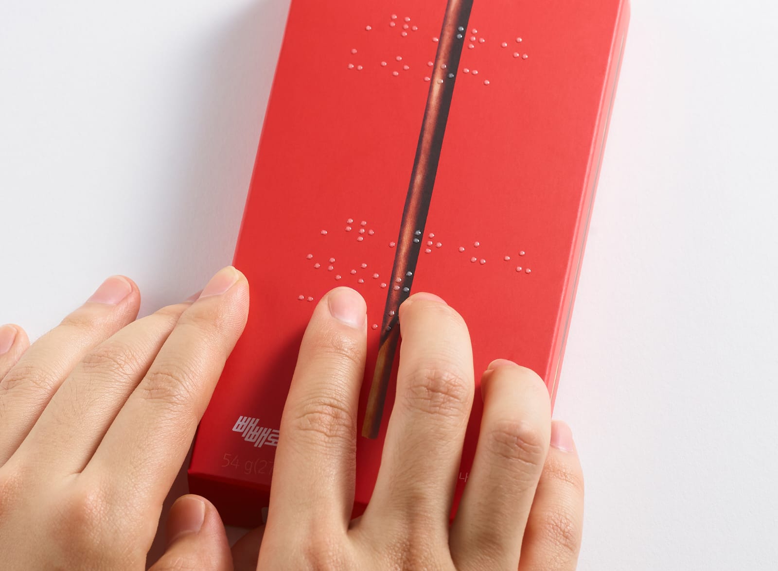 Se muestra parte del envase color rojo unas manos leyendo la inscripción en braille: “Comparte tu corazón con Pepero”